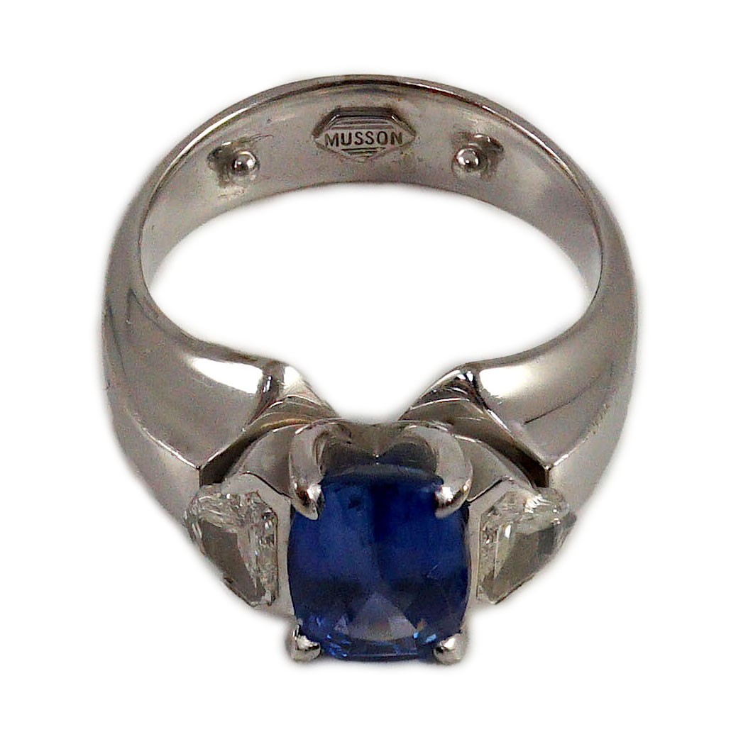 A modern white gold (tests as 18ct), single stone oval cut Ceylon sapphire and two stone shield cut diamond set dress ring, by Musson